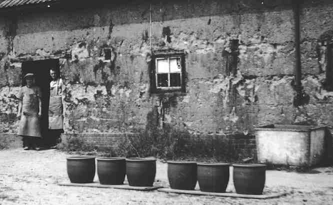 Two potters standing in the doorway of a cobb built workshop.